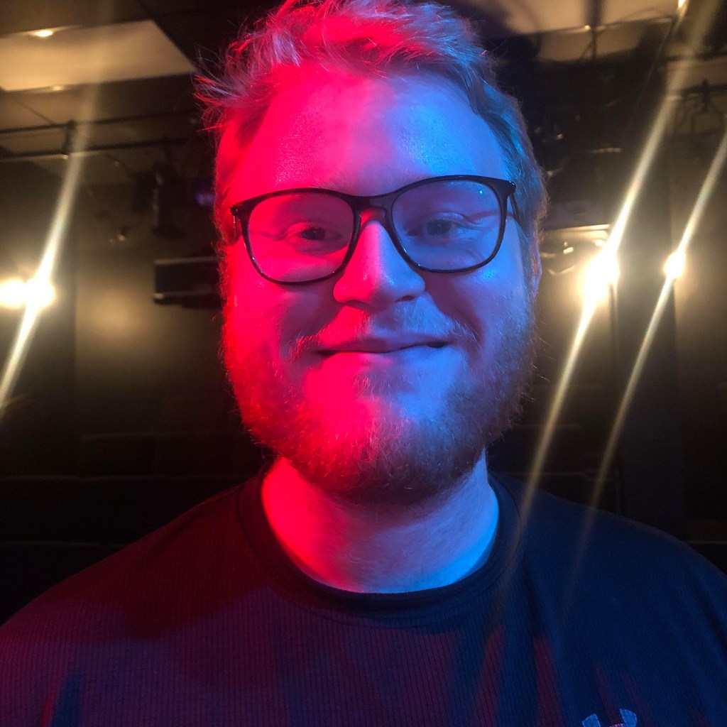 Picture of me covered in blue and red light in a theater in 2019 when I directed a play about the Internet.