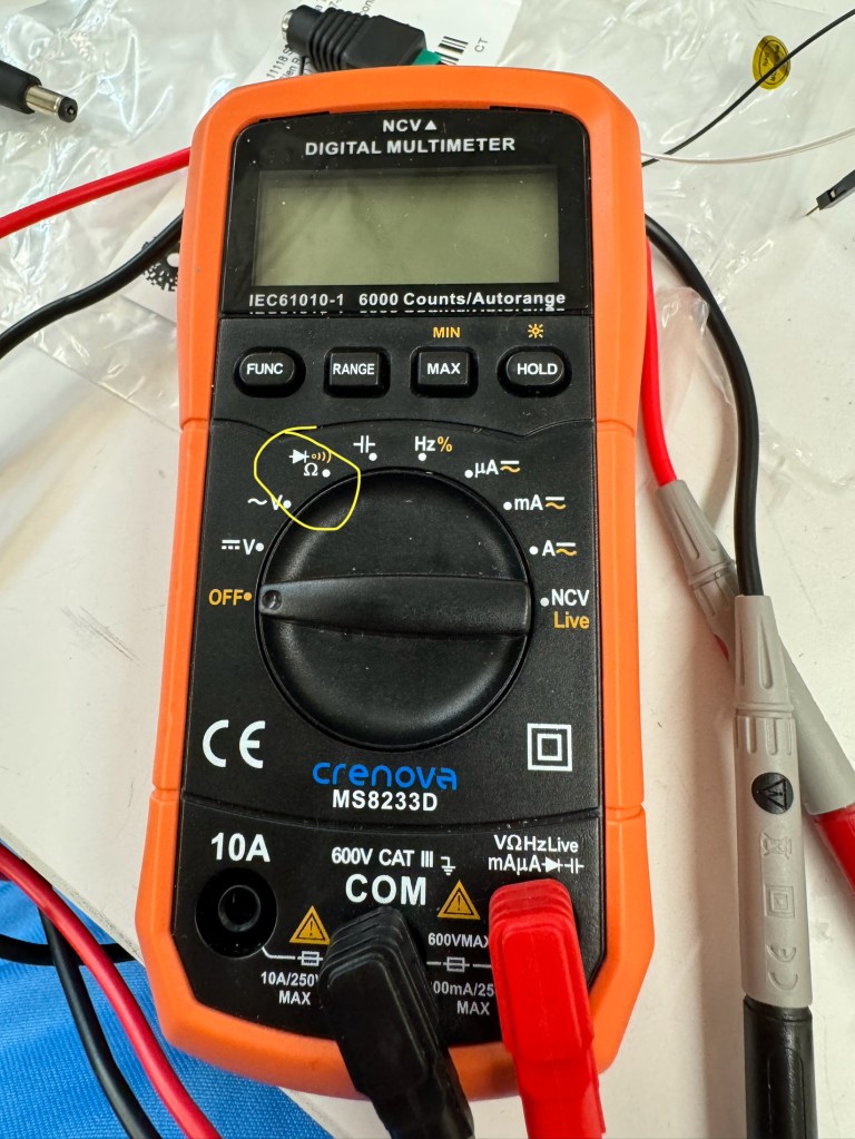 An orange multimeter with a yellow circle over the setting for Continuity/Resistance testing